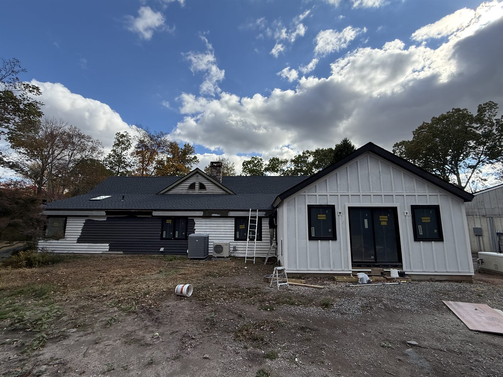 Rear elevation of a house before painting, showing white siding, a partially coated dark section and a board-and-batten addition