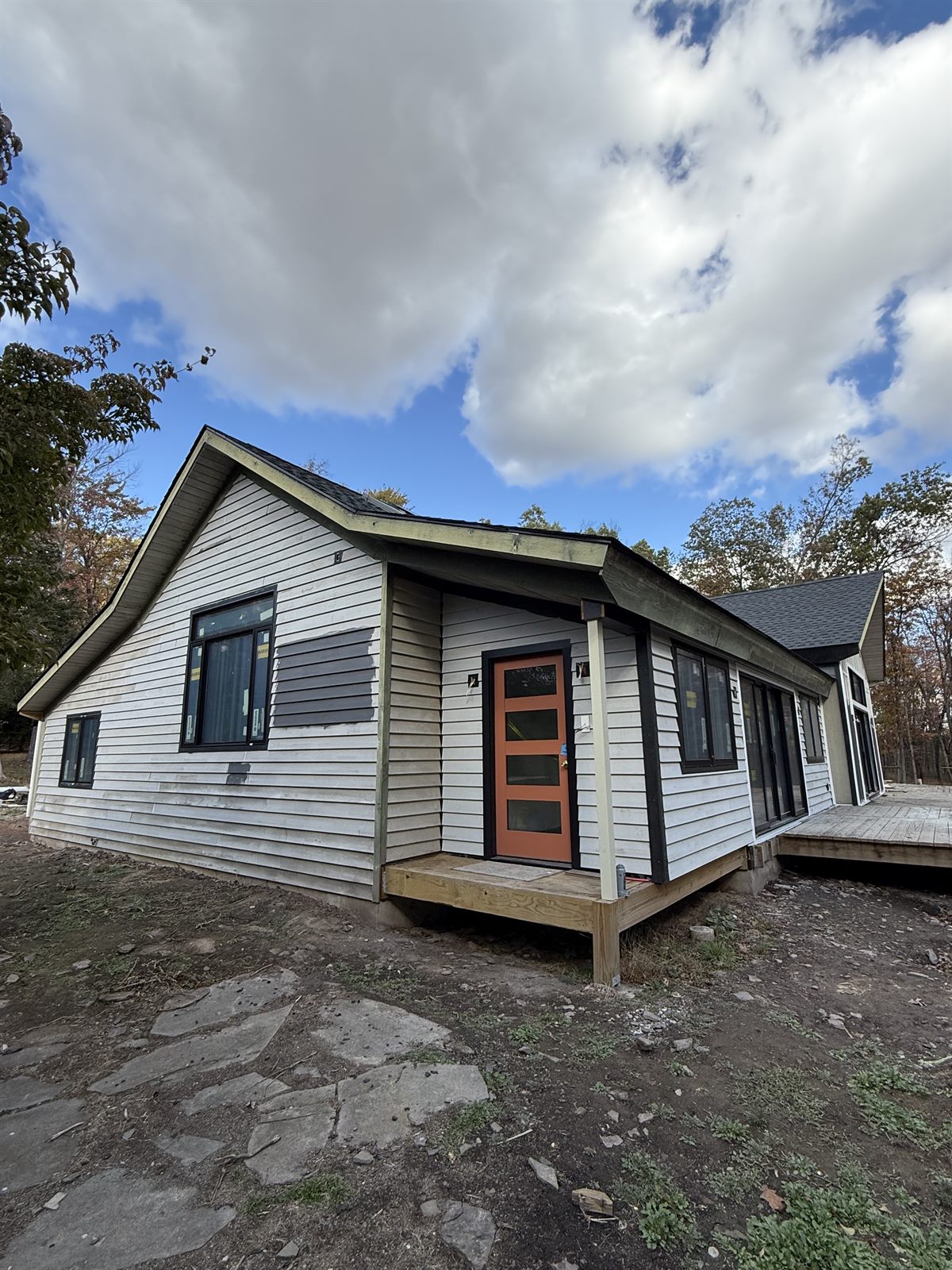Front corner of a house before painting, with weathered white lap siding, exposed patched panels and a wood-framed porch
