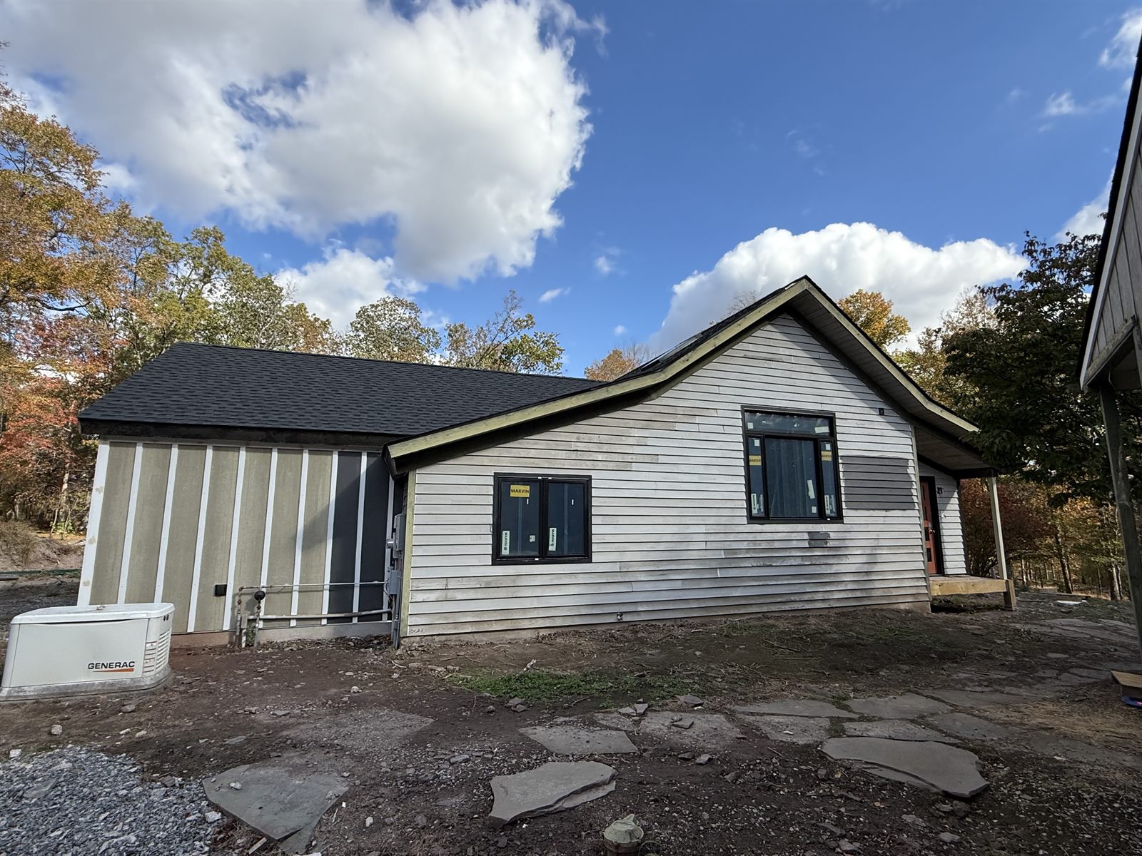 Side of a house before painting, with pale weathered siding and an unfinished board-and-batten wing